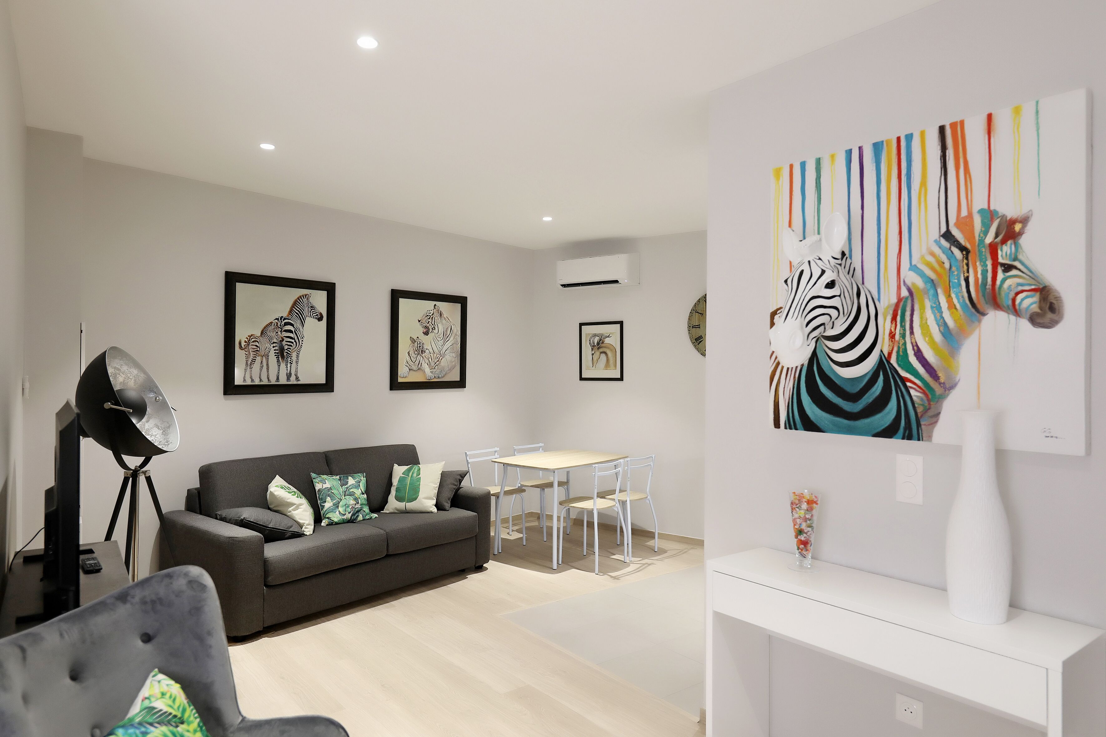 A modern living room with a grey sofa, a white dining table, and a large zebra painting on the wall.