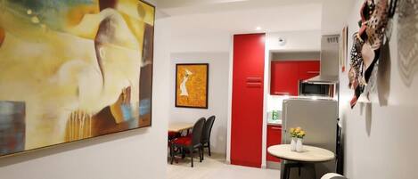 Una sala moderna con un cuadro abstracto grande, un comedor con sillas y una cocina con detalles en rojo.