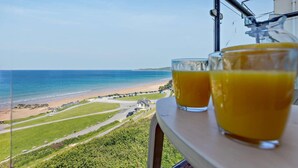 Un balcon avec vue sur la plage et deux verres de jus d’orange.