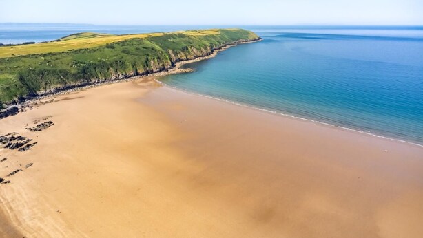 Un paysage côtier avec une plage de sable, des zones herbeuses et une vue dégagée sur l’océan.