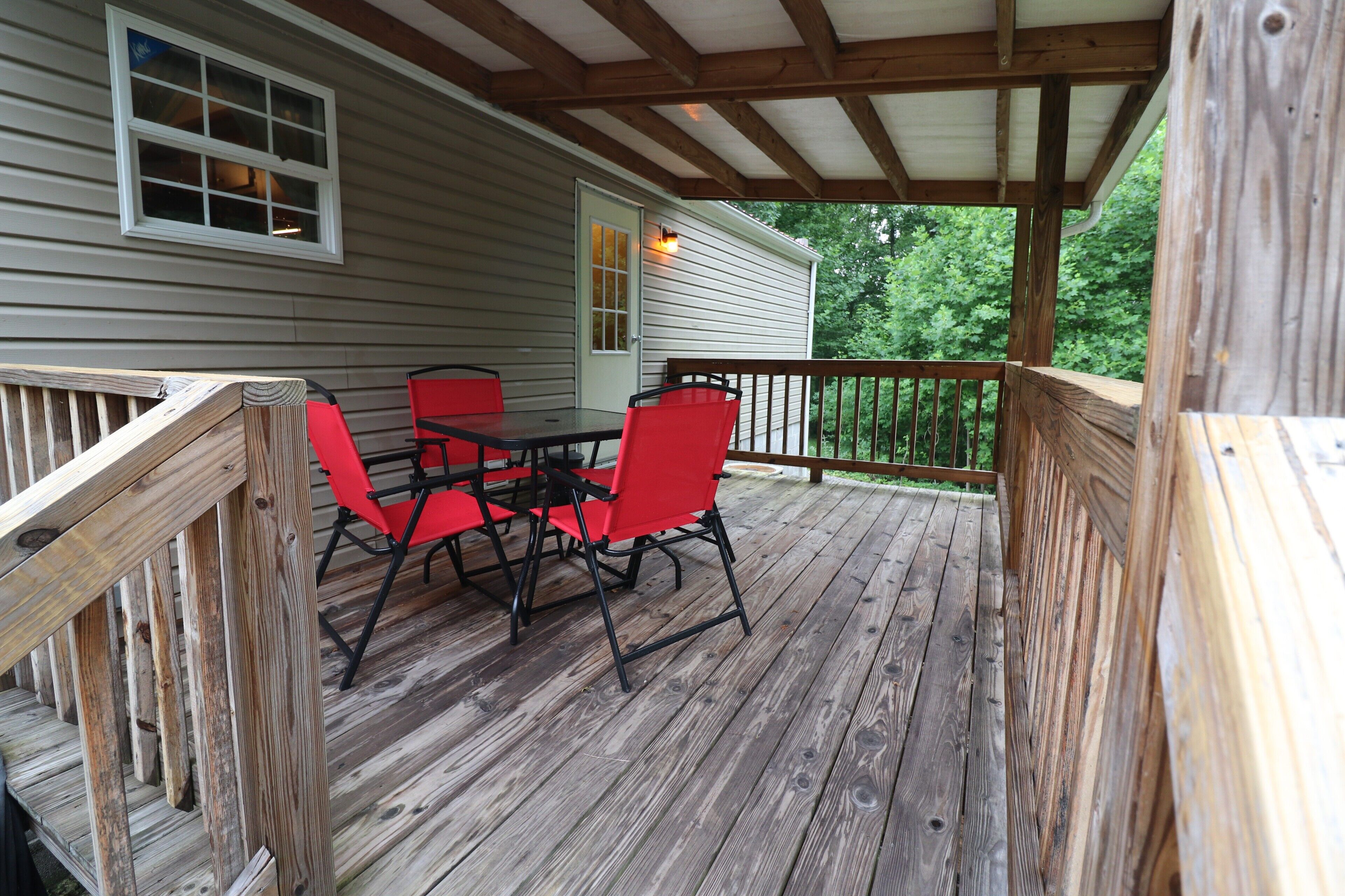 Une terrasse en bois avec une table et des chaises rouges, une balustrade en bois et une maison en arrière-plan.