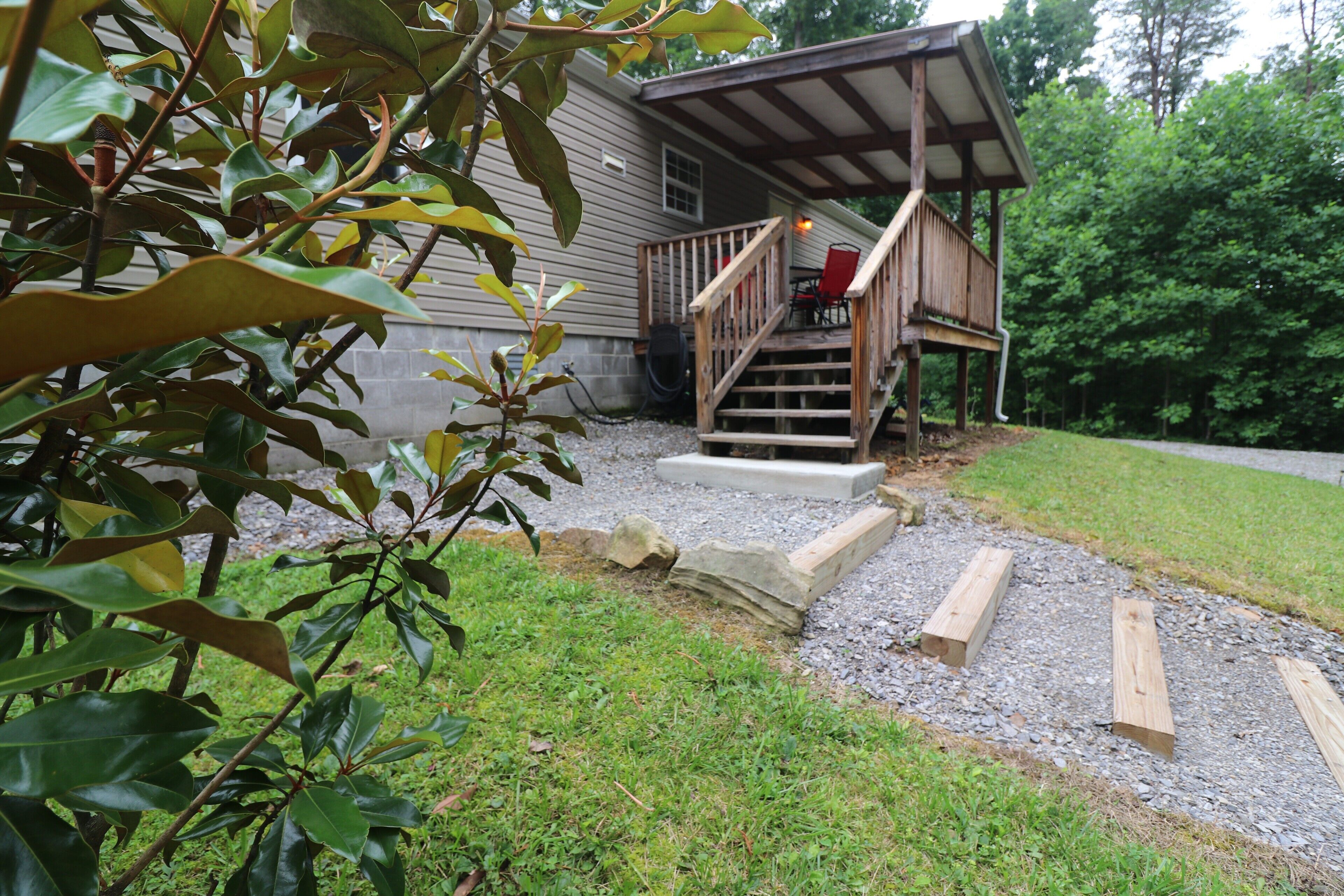 A wooden cabin with a porch, gravel pathway, and surrounding greenery.