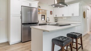 Una cocina moderna con armarios blancos, electrodomésticos de acero inoxidable y una isla central con taburetes.