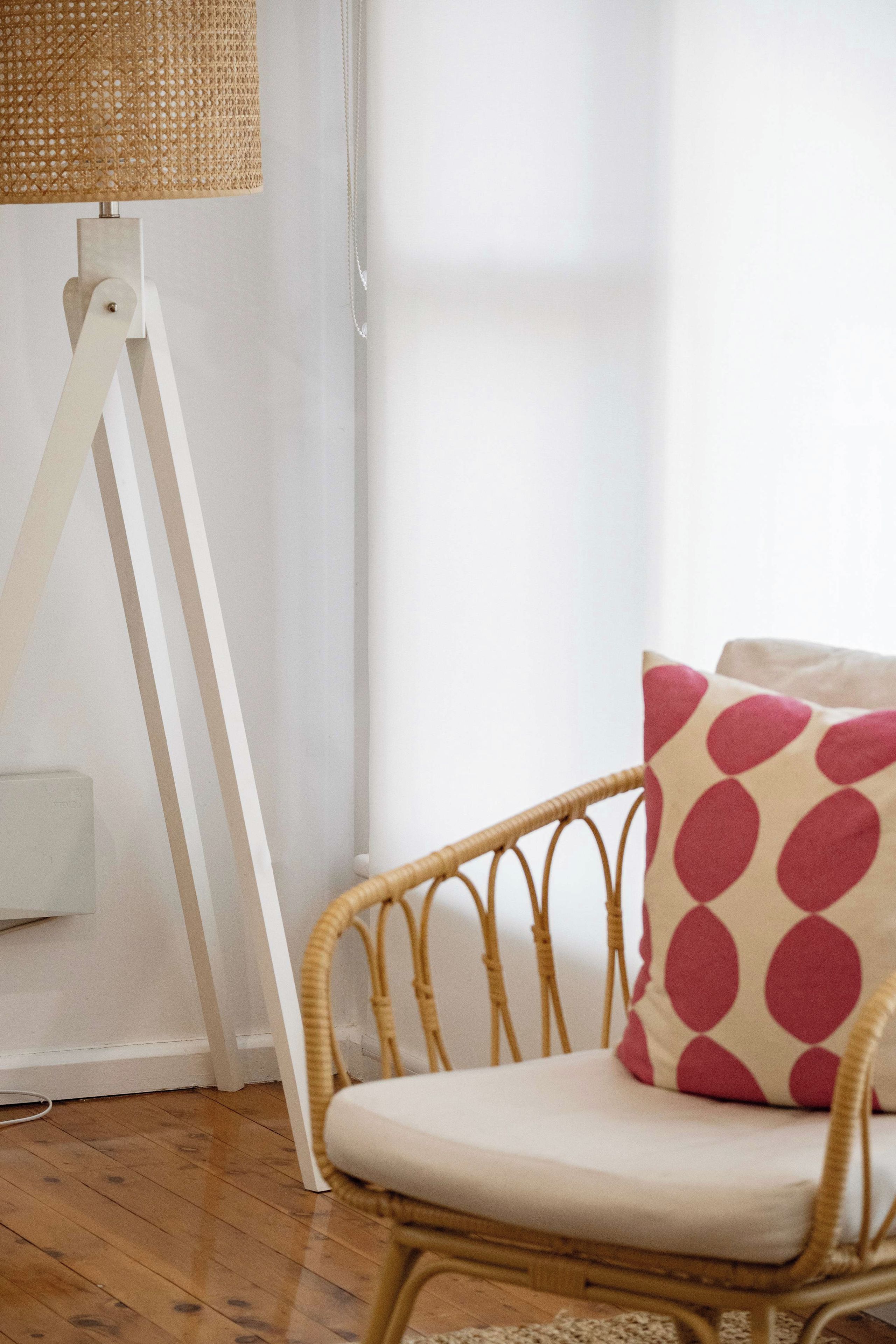 A wicker chair with a cushion, a white floor lamp, and a window with sheer curtains.