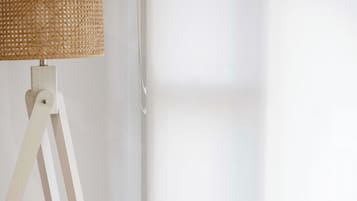 A wicker chair with a cushion, a white floor lamp, and a window with sheer curtains.
