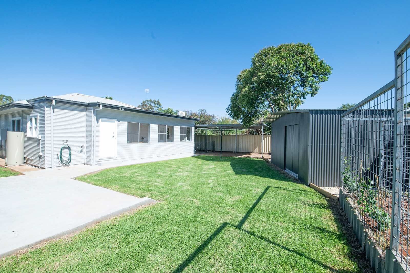 Une propriété résidentielle dotée d’une cour arrière clôturée, d’un garage séparé et d’un grand arbre.
