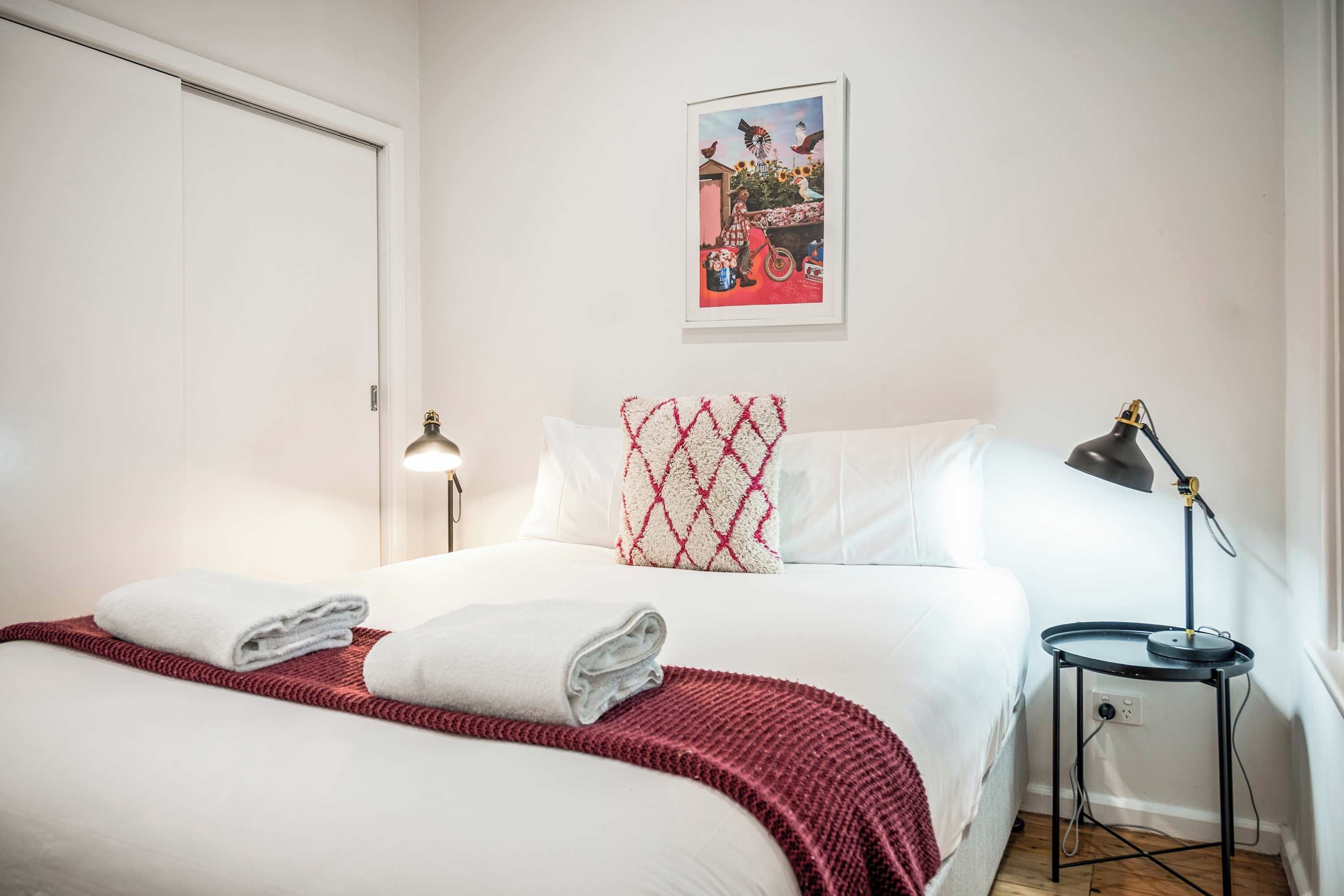 Habitació d'hotel amb un llit, una làmpada de nit, una taula petita i un quadre penjat a la paret.