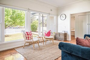 A bright room with large windows, a wicker chair, a blue sofa, and a wicker chest of drawers.
