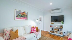 A living room with a white sofa, a TV, and a bookshelf. - Cobbora Cottage -  Sleek & Stylish, Near Hospital (Dubbo)