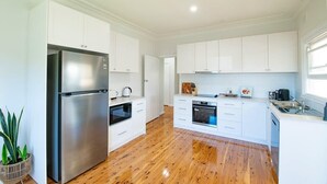 A modern kitchen with white cabinets, stainless steel appliances, and a wooden floor. - Cobbora Cottage -  Sleek & Stylish, Near Hospital (Dubbo)