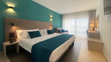 Una habitación de hotel moderna con una cama grande, dos mesitas de noche, un escritorio y un amplio ventanal con cortinas.