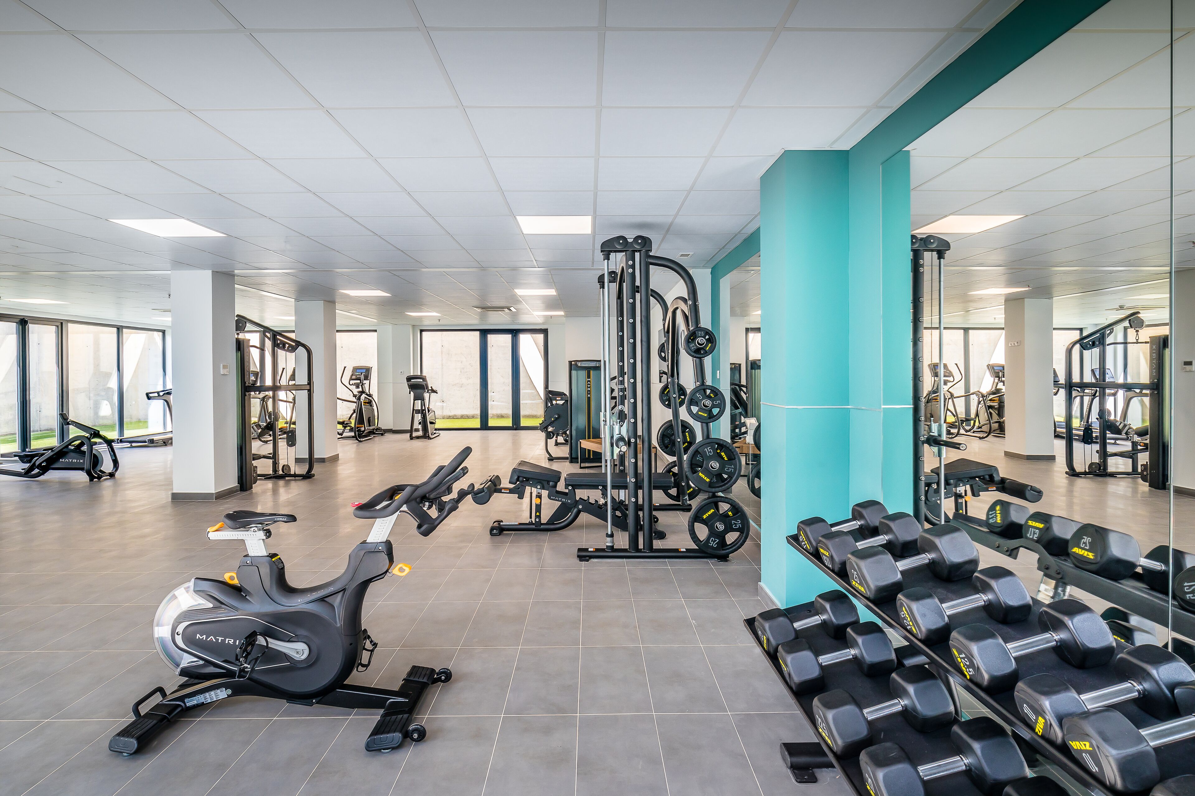 Un gimnasio con equipo de ejercicio, un espejo grande y una pared de acento color turquesa.