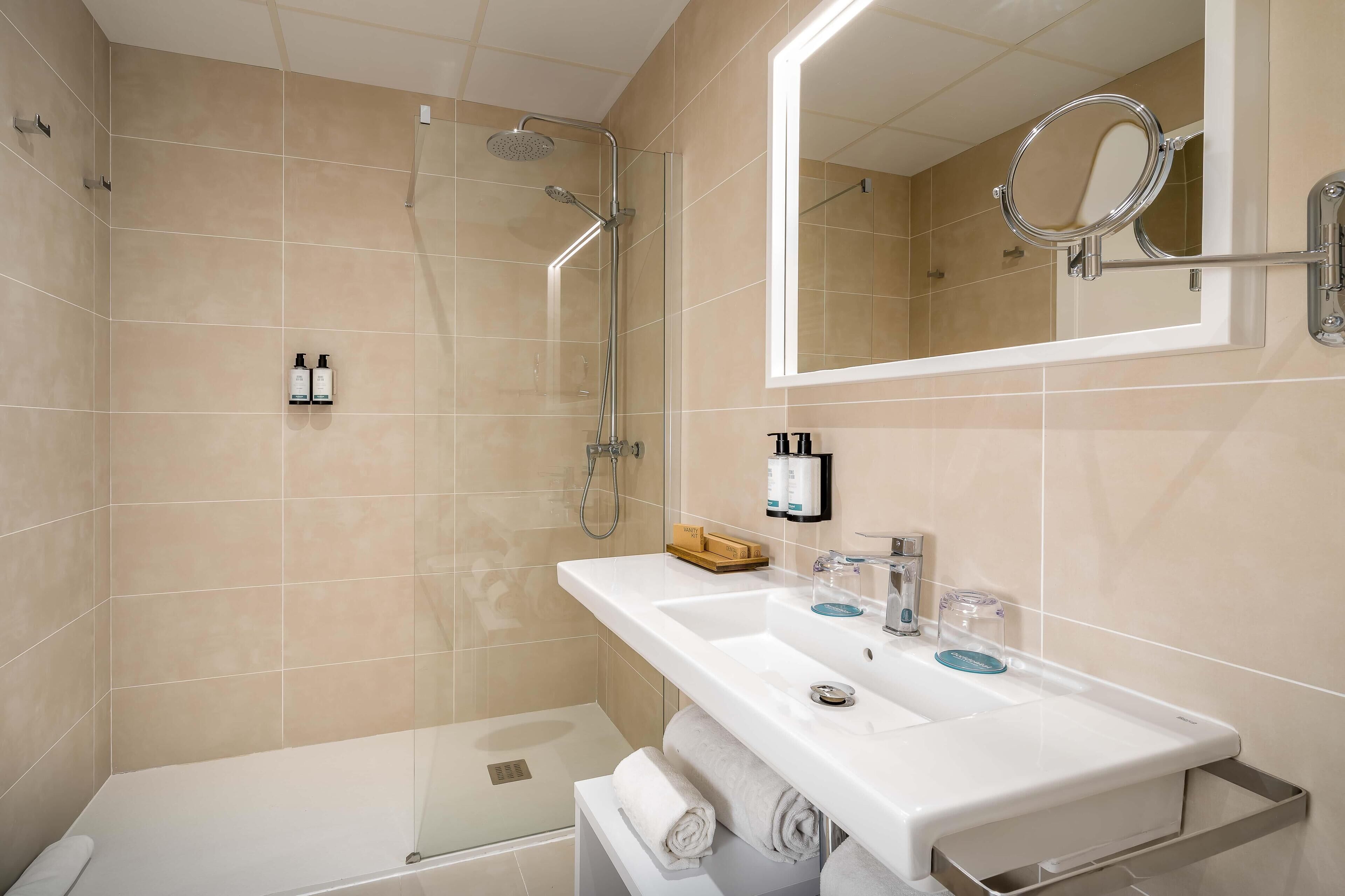 A modern bathroom with a glass-enclosed shower, a large mirror, and a white sink with toiletries.