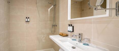 A modern bathroom with a glass-enclosed shower, a large mirror, and a white sink with toiletries.