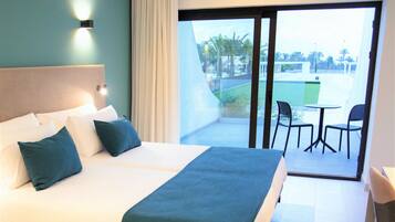 Habitación de hotel con una cama grande, vistas del exterior a través de una puerta corredera y una pequeña mesa con sillas.