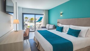 A modern hotel room with a large bed, a desk, and a view of a pool and palm trees. - Occidental Mar Menor (Cartagena)