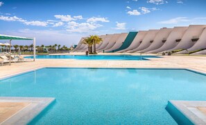 Una piscina con un moderno fondo arquitectónico, rodeada de sillas de descanso y palmeras.