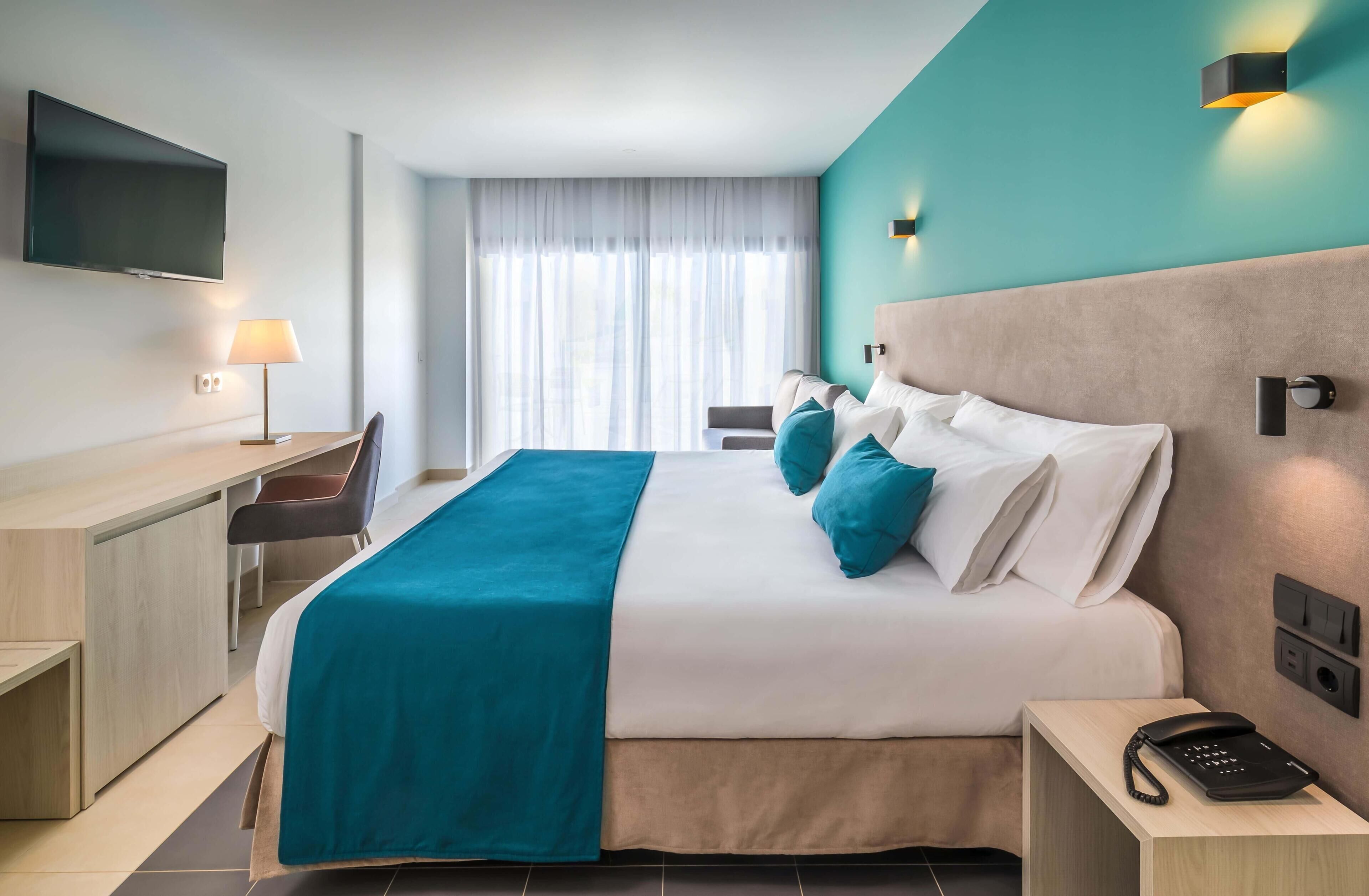 A hotel room with a bed, desk, chair, and a TV mounted on the wall.
