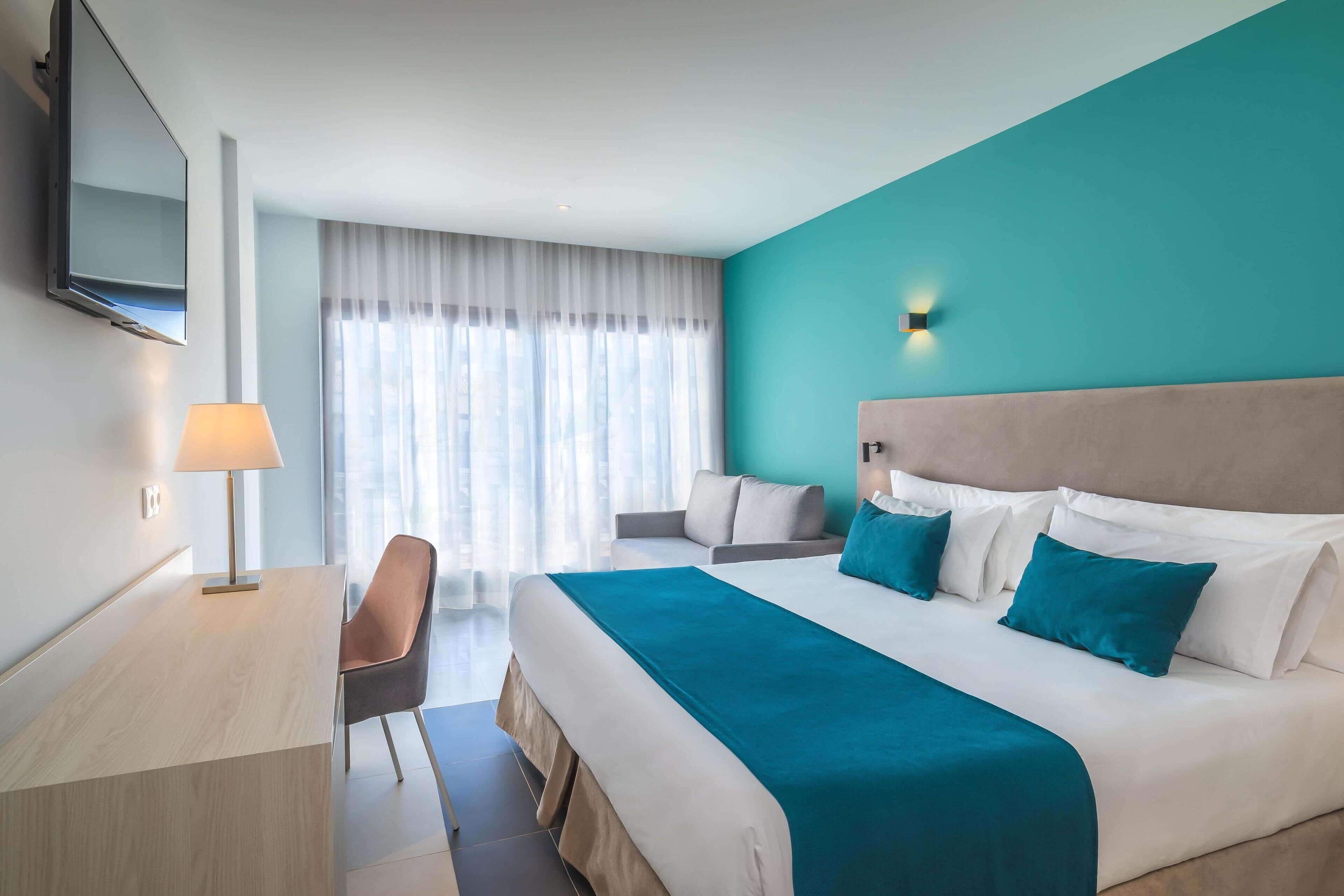 Ein Hotelzimmer mit einem großen Bett, einem Schreibtisch, einem Stuhl und einem Fernseher.