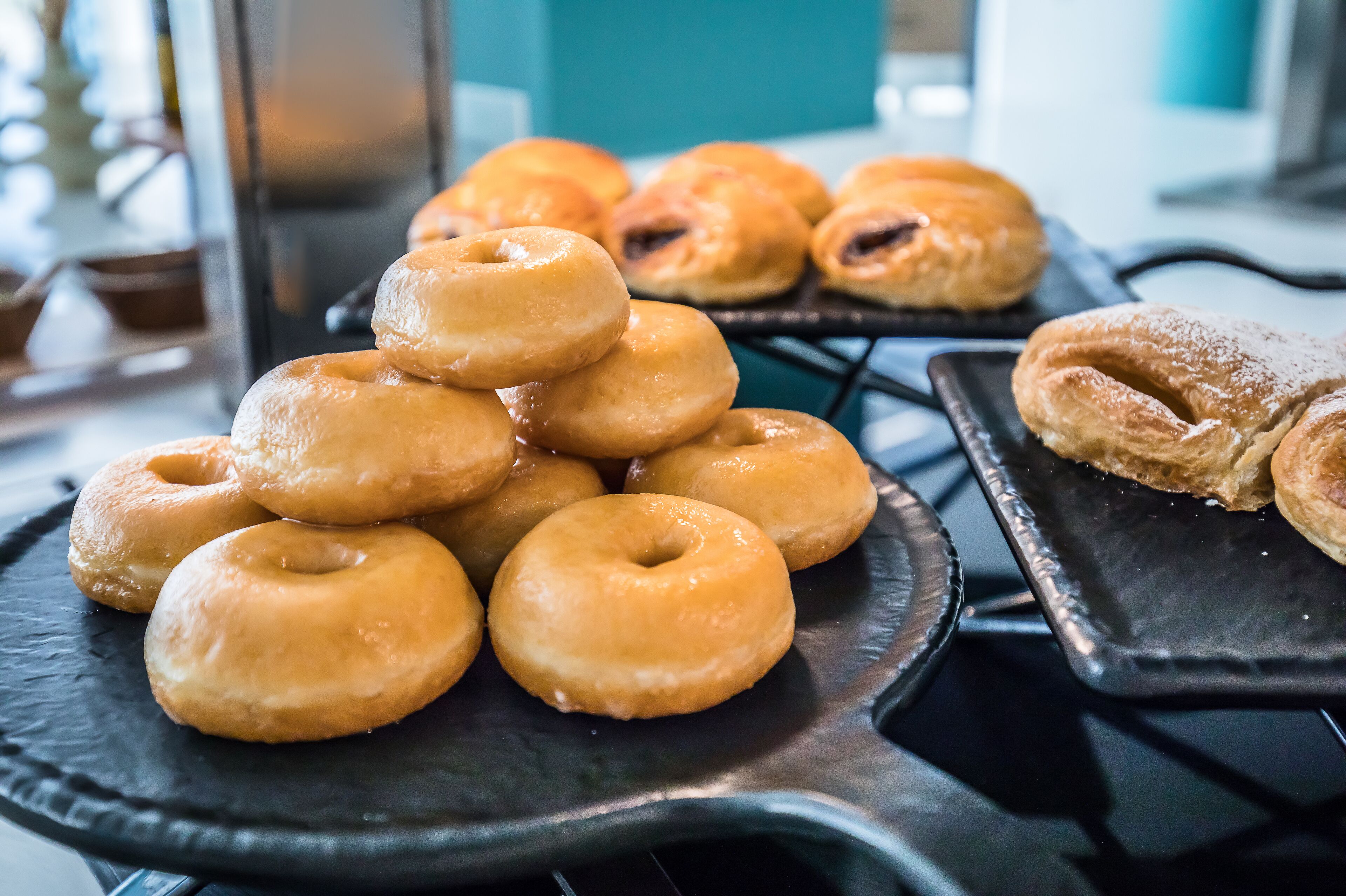A variety of pastries on trays, including donuts and pastries, displayed on a counter.