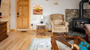 A cozy living room with a wooden floor, a stone fireplace, a beige armchair, a wooden coffee table, and a patterned rug. - Minutes to Canandaigua Lake Boat Launch, Fireplace, Large Yard, Hiking (Naples)