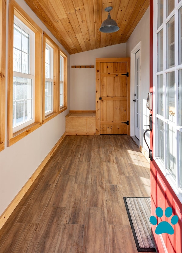 A hallway with wooden flooring, large windows, and a wooden door.