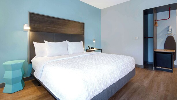 A modern hotel room with a large bed, a bedside table, and a small stool. - TRU BY Hilton Wake Forest Raleigh North (Wake Forest)