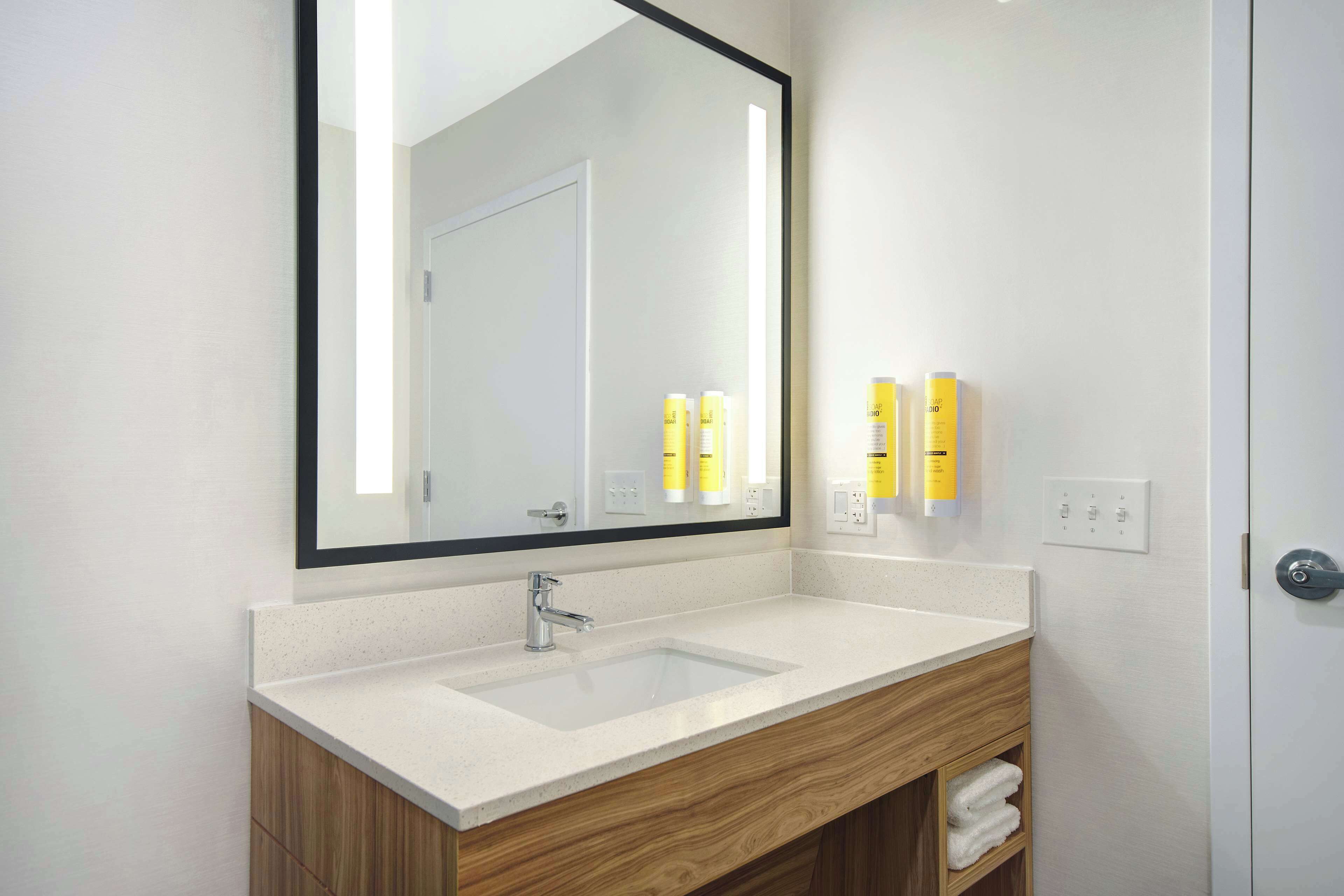 A modern bathroom with a white sink, wooden vanity, and a large mirror.