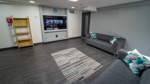 A modern living room with a grey sofa, a wooden shelf, a flat-screen TV, and a skylight. - Homely Studio Next to City Centre (Birmingham)