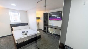 A hotel room with a bed, a desk, a chair, a TV, and a mirror. - Homely Studio Next to City Centre (Birmingham)