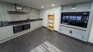 A modern kitchen with a built-in oven, a microwave, and a coffee maker. There is a wooden ladder leaning against the wall and a digital screen displaying property listings. - Homely Studio Next to City Centre (Birmingham)