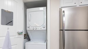 A compact kitchen with a stainless steel refrigerator, a washing machine, and a microwave.