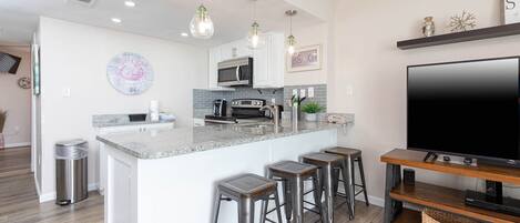 Una cocina moderna con una isla central, taburetes de bar, un televisor de pantalla plana grande e iluminación colgante.
