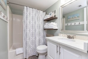 Une salle de bain avec un rideau de douche, des toilettes, un lavabo avec un miroir et un porte-serviettes.
