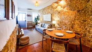 A dining area with a stone wall, a wooden table set for four, and a woven chair.
