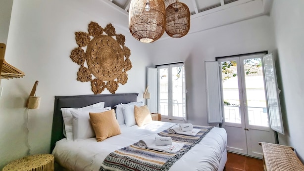 A spacious bedroom with a large bed, a decorative wall hanging, and a view of the outdoors through the windows.