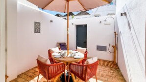 A small, enclosed patio with a round table, red wicker chairs, and a large umbrella.
