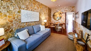 A living room with a stone wall, a blue sofa, a dining table, and a TV mounted on the wall.