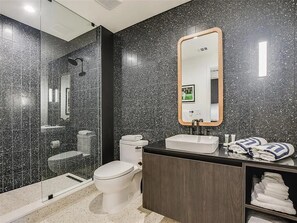 A modern bathroom with a glass-enclosed shower, a white toilet, a vanity with a mirror, and neatly folded towels. - Soak in Iconic City Views from the Heart of Austin – Rainey Street Luxury Studio (Austin)