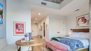 Ein modernes Schlafzimmer mit einem hölzernen Bett, einem runden Tisch, einer rosafarbenen Bank und Blick auf das Treppenhaus.