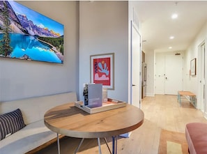 A modern hotel room with a wooden floor, a round table with a welcome sign, a large painting of a mountain landscape, and a colorful abstract artwork on the wall. - Soak in Iconic City Views from the Heart of Austin – Rainey Street Luxury Studio (Austin)