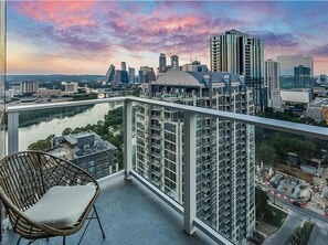 A balcony with a view of a city skyline at sunset, a wicker chair, and a glass railing. - Soak in Iconic City Views from the Heart of Austin – Rainey Street Luxury Studio (Austin)