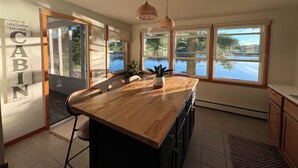 A kitchen with a wooden island, large windows, and a 'Welcome to our Cabin' sign.