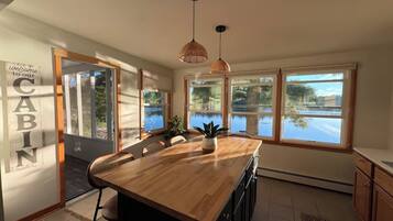 A kitchen with a wooden island, large windows, and a 'Welcome to our Cabin' sign.