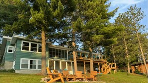 A two-story house with a deck, surrounded by trees and a grassy yard.
