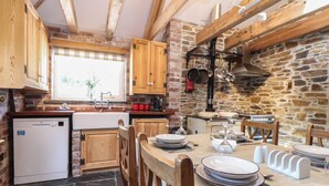 Une cuisine rustique avec des meubles en bois, un mur en pierre et un coin repas où une table est dressée pour quatre personnes.