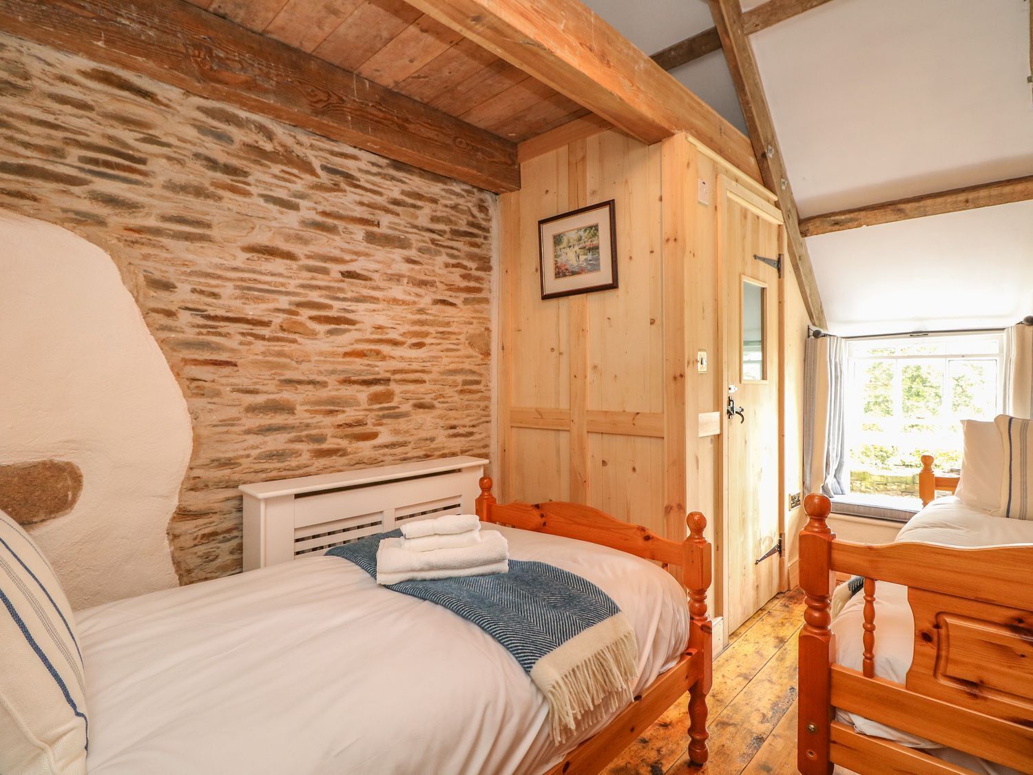 A bedroom with two wooden beds, a stone wall, and a wooden wardrobe.
