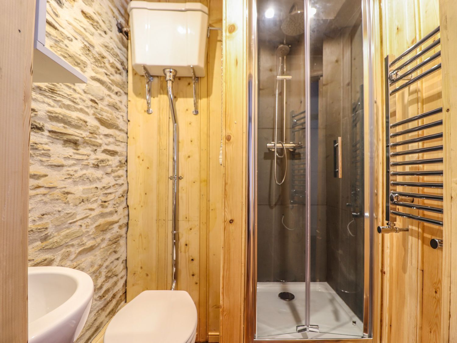 Een houten badkamer met een stenen muur, een toilet en een douchecabine met glazen wanden.