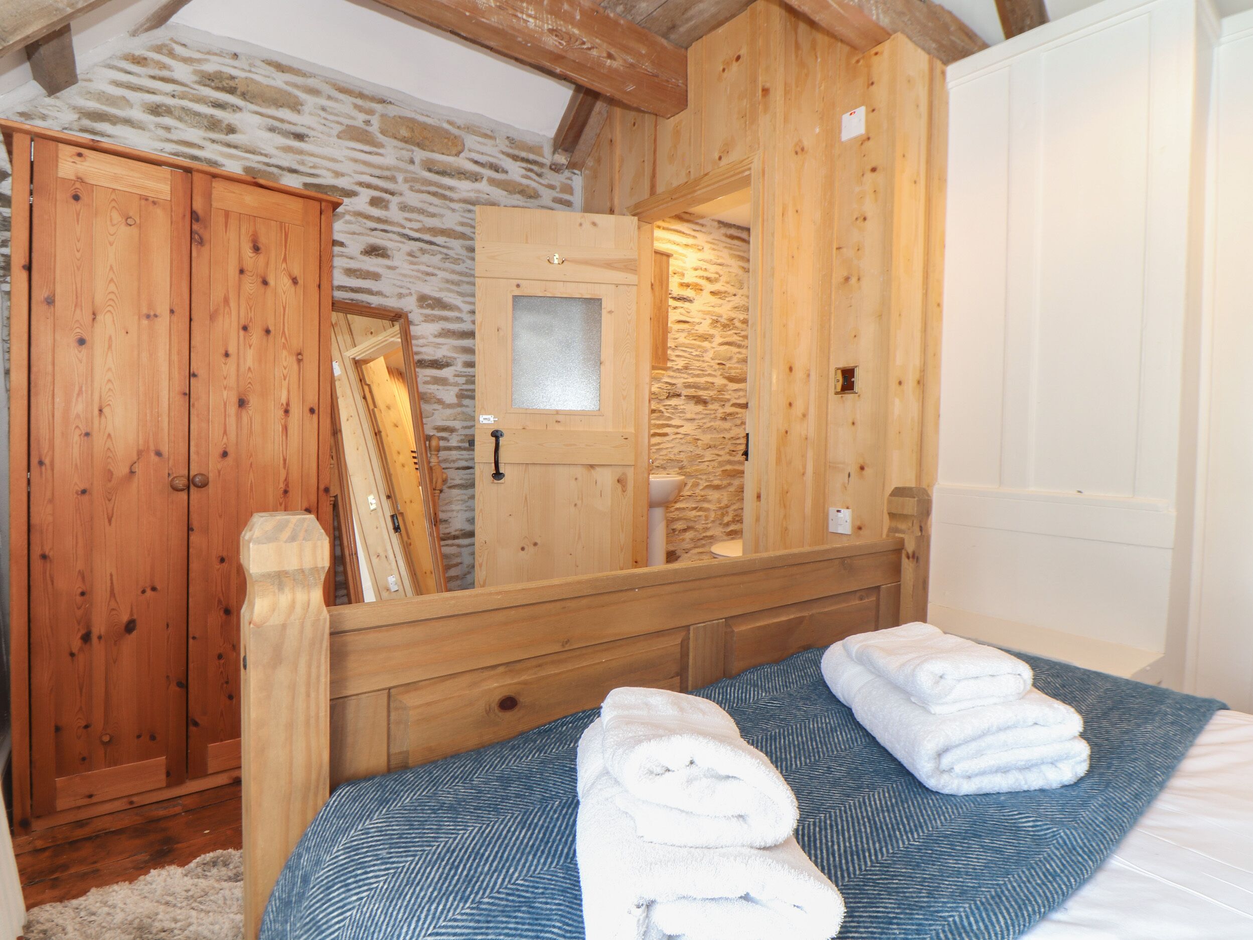 Une chambre à coucher en bois avec un mur en pierre, une armoire en bois, un miroir et un lit avec des serviettes.