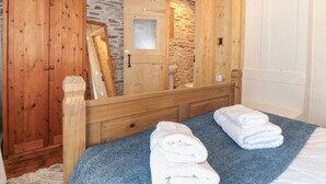 Une chambre à coucher en bois avec un mur en pierre, une armoire en bois, un miroir et un lit avec des serviettes.
